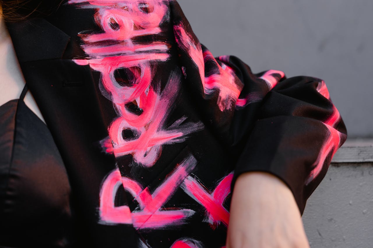 Detailed close-up of a black blazer with vibrant hand-painted abstract art design in pink.