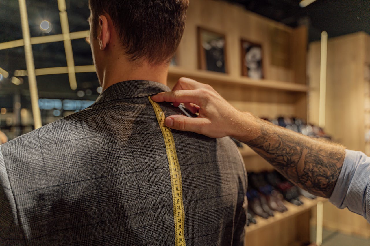 A tailor measuring a clients back with a tape inside a clothing store for a bespoke suit fitting.